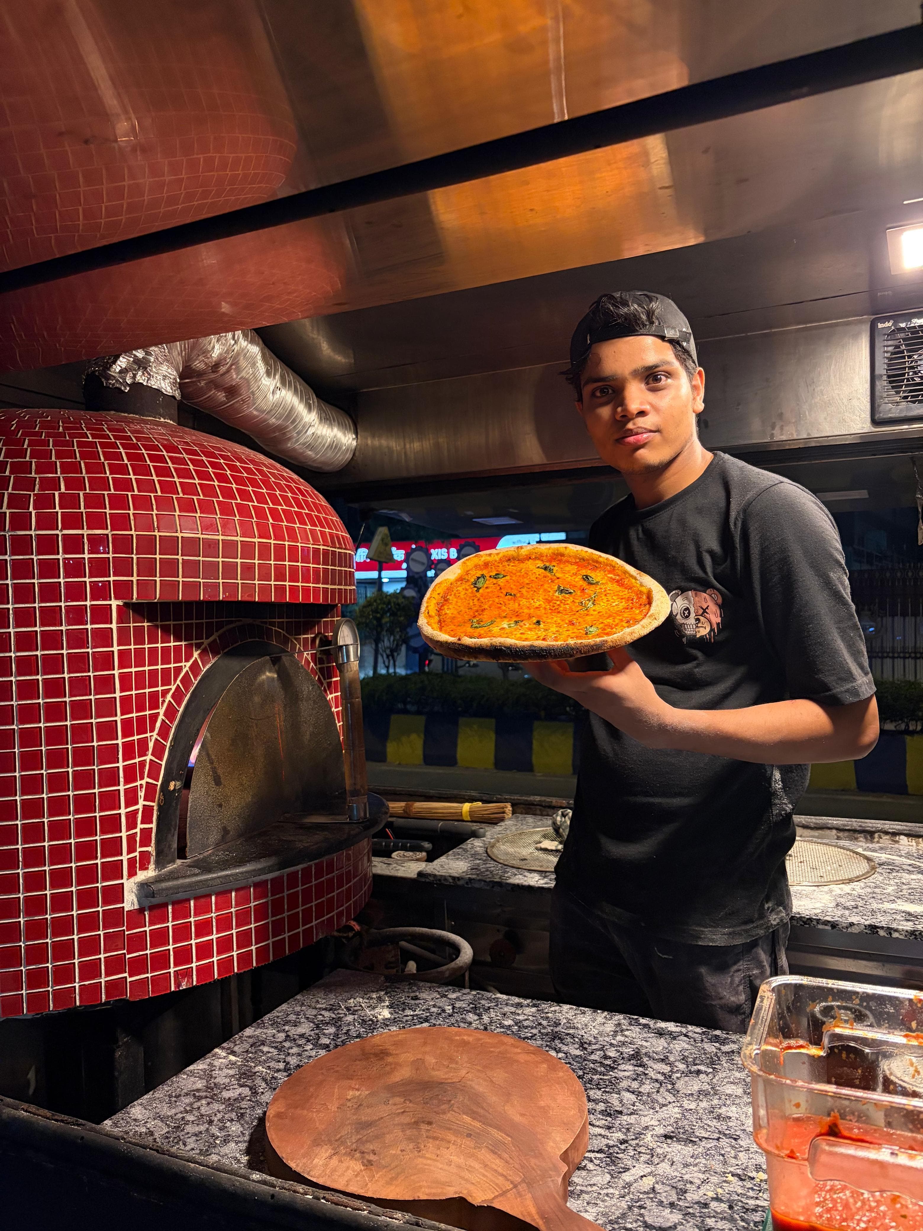 Pizzaiolo proudly presenting freshly baked Neapolitan pizza from the oven